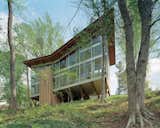 The house is perched on nine broad wood trusses to avoid cutting a single tree. The trusses also permit air and water to flow under the house, preserving the hydrology. The butterfly-shaped roof opens views to the creek and funnels rainwater into a collection system.