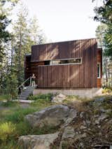 The facade is clad with beveled siding, stained dark to meld into the forest.
