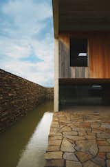 Protected by a natural stone roof, the mortuary’s upper half comprises a smooth oak cube contrasted with the quarried stone surrounding walls and floor. The architects conceived the water feature as a “golden water surface [that serves as] a meditative focal point.”