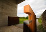 Cor-Ten steel doors open to the gravel path that meanders through a flowering meadow to the cemetery.