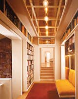 A hallway ends in a built-in bookshelf and a banquette backed with brass.