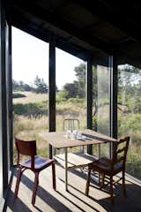 The screen porch serves as an auxiliary dining area and is furnished with a Teak outdoor table from Ikea surrounded by three chairs, including two vintage chairs and a silver 1006 Navy chair by Emeco from Design Within Reach.