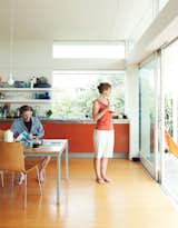 This bach in New Zealand was designed with a combined open-plan kitchen, living room, and dining area, for which homeowner and architect Gerald Parsonson designed a dining table that seats ten. Bare bulbs, open shelves, and bright orange MDF cabinets in the kitchen maintain the low-key vibe.