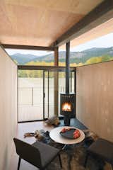 A compact interior with a black fireplace feels simultaneously cozy and boundless, with floor-to-ceiling glass doors that open out to views of the mountains of Washington state. The cork flooring, weathered steel, and wood walls contrast with the raised, open ceiling for the perfect mix of warm and minimalist, open and enclosed.