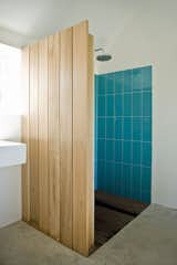 Colored tiles in the shower are revealed behind a cedar wood wall. "The sound of falling water on wood and the surrounding fields form the background," say the architects. "This was our way of introducing an immaterial idea of what luxury actually could be about."