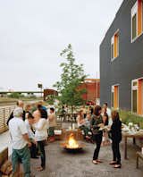 Outdoor, Large Patio, Porch, Deck, Stone Patio, Porch, Deck, and Planters Patio, Porch, Deck Architect Douglas Stockman says the building's charcoal-and-orange exterior coloring was "intended to reflect the dynamic character of the neighborhood." Here, it provides a festive backdrop to the residents' semi-annual Finn Lofts community party.  Photo 5 of 7 in Inspiring Examples of Multifamily Living by Brandi Andres from Building Community