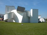 The Vitra Design Museum is housed in this iconic building by Frank Gehry. Built in 1989, it's the earliest non-factory structure on campus. The factory and the gate that he built in tandem with the museum all share the the same aesthetic: white walls, dark roofs, a square structure on one side, and a round form on the other. Though the white walls stand out in the landscape on a bright fall day, the color was specified in order to help it blend in with surroundings. The land on which the Vitra Campus is located is a cherry field and when the flowers bloom, the building disappears among the pale pink and white flowers.  Photo 4 of 13 in Touring Vitra Campus, Part 1 by Miyoko Ohtake