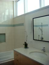 The bathroom features recycled countertops by IceStone. The low-flow sink faucet and the Croma E 75 shower fixture (visible in the mirror) are by HansGrohe. The tile in the shower is by Horus.