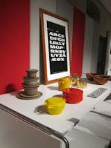 In the foreground, a red Kobenstyle and yellow Orecast pot, designed by Jens Quistgaard in 1954 and 1959, respectively, with an alphabet poster in the background by Claus Achton Friis.