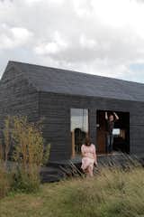 Exterior, Barn, Cabin, Saltbox, House, and Wood Carl Turner and Mary Martin pose on the porch of the Stealth Barn, a multipurpose structure that plays as a guest cottage, office space, and escape from whatever may be cooking at Ochre Barn.  Exterior Cabin Wood House Saltbox Photos from A Pair of English Barns Hide Unabashedly Bold and Budget-Friendly Minimalist Interiors