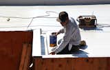 A roof installer from J.T. Harris finishes installing the Versico PVC membrane on a garage roof parapet. The parapet will have a black metal coping installed as the final finish.