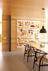 An abstract painting by Michael Young complements the glow of the dining room’s pine walls. A collapsible silicone lampshade by Swedish designers Form Us With Love for Muuto hangs above a Macek Furniture Company table.