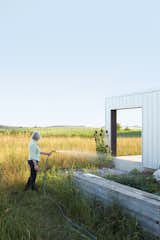 Outdoor, Grass, Gardens, Garden, and Field Maggie Treanor waters plants around her rural home.  Search “homeowner manages his house anywhere” from A Sustainably Built Home in Rural Ontario