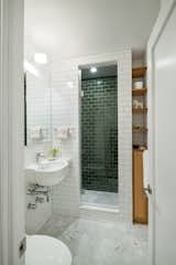 An updated bathroom features a mix of tiles: Carrara marble tiles on the floor, green subway tiles from Heath Ceramics on the inner shower walls, and white subway tiles from Daltile on the exterior walls. The fixtures are from Grohe.