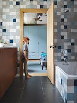 Bath Room and Ceramic Tile Wall Rock stands in the doorway to the boys’ bathroom, which is lined with semi-gloss Modern Dimensions tiles from Daltile. “We wanted it to be playful,” Hufft says, “so we chose each color and laid out the tile distribution in Photoshop.”  Photo 10 of 13 in BATHROOM IDEAS by Dana from This Kansas City Home Looks Like Its Neighbors, But Reveals a Truly Modern Sensibility