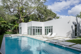 A pool and outdoor shower fixture were added during the renovation. Shadows from nearby palm trees cast dramatic silhouettes on the blank canvas of a house.