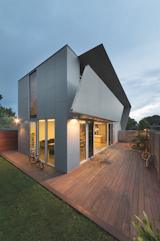 The family built the rich wood deck in the backyard, a warm visual contrast to the cold concrete and steel building. On the south side, a carefully concealed shed houses more bicycles and tools.  Photo 5 of 7 in Daring Geometric Houses Around the World by Diana Budds from Angular Australian House Fits a Family’s Active Lifestyle