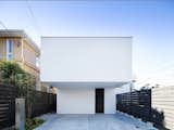 The façade designed by Apollo Architects and Associates features an overhanging upper level, which ensures that the entrance is pleasantly shaded and demarcates the property’s two parking spaces. The home’s wooden structure is clad in a bright white exposed concrete.