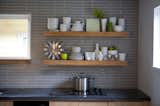 Rolling up the sleeves done right! Dishes rest atop a shelf made from a type of textured lumber typically used for framing. The horizontal tile behind the shelf echoes the pattern and proportion of the bricks used in the hearth. The residents did nearly all of the work themselves in this DIY Seattle renovation, which was often a learning experience. "We had to be willing to roll with the punches. A dimple in the concrete counter isn’t a mistake—it adds character."