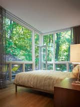 The bedroom features floor-to-ceiling windows. The flooring in the room, as throughout the house, is bamboo.