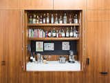 A wall of custom floor-to-ceiling walnut cabinetry in a kitchen in San Francisco includes a built-in bar, complete with its own shelves and counter space. The cabinet doors of the bar fold back into their frames so that the space can act like as an open niche when guests are over.
