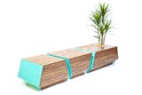The indoor/outdoor bench posesses modern form, high-quality materials, and expert craftsmanship. The blue powder-coated steel ends and walnut slats are attached to an endoskeleton without any visible hardware, and the stainless steel planting pot sets off the plants within.