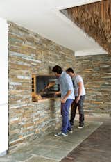 Achilleas and his friend Jovi tend the grill, which was Achilleas’s own design and is supported by a concrete beam—cast with slate stones embedded in it—just above the opening.