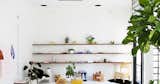 Various goods hang out on long wooden shelves mounted on the wall with plenty of natural light infiltrating in to the right. Photo via Table of Contents.