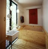 The traditional Japanese bathroom is located just off the central passageway between the two parts of the house. The couple wash here before bathing and relax in the wood-lined onsen, or tub.  Photo 4 of 7 in This Japanese-Style Box Home Boasts a Two-Story Bookcase