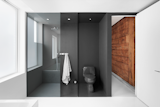 A original hemlock wood wall clads the corridor leading to the bathroom. Just inside, the dark gray epoxied shower area (with a Cimarron Kohler toilet) forms a solid contrast to the white walls and floors.