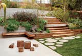 A backyard garden with varying-sized circular cement stepping stones, wood stairs, and an elevated planter filled with California-native plants. 