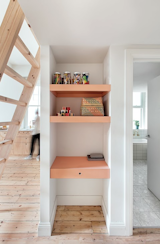 Whimsical salmon accents play favorably against the pine floors and plywood joinery. A ladder in the living room leads up to a mezzanine loft guest room while also creating a compact work nook below.