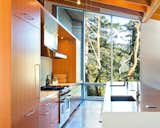 Light streams in through the kitchen from massive, floor-to-ceiling windows that offer peaceful views of the outside foliage.