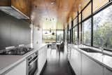 In the kitchen, a Blanco exhaust fan is surrounded by a stove, oven, and dishwasher by Westinghouse. A series of pendants by She Lights are equipped with LED fittings.