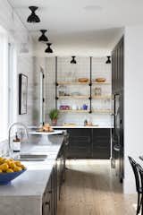 This space combines black cabinets, white subway tiles, marble countertops, and wooden floors to create a balance between rustic warmth and industrial simplicity.