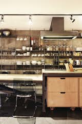 The kitchen worktop is framed in iron, and functional wheeled storage fits perfectly underneath. The full-wall shelving system offers ample storage for dishware and cooking accessories.