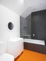 Low-maintenance, sustainable materials were favored throughout the house. Striking orange Pirelli studded rubber floors were chosen for the main bathroom. Clean white fixtures and black shower cladding complete the graphic space.