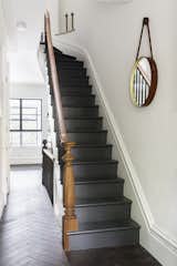 Reclaimed oak with a custom finish by LV Wood surrounds a staircase in a herringbone pattern. The new stairs are painted off black by Farrow & Ball, and the handrail that lines them is of salvaged mahogany.