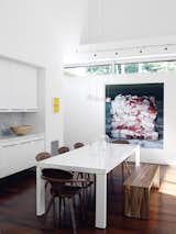 A white lacquer Ligne Roset dining table is joined by a wood bench from Room &amp; Board and bent-plywood Cherner chairs. Baconcube 4 by Cindy Wright hangs on the wall.