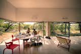 The dining room, adjacent to the living room, features expansive openings and an oval dining table with mixed-color plastic chairs.  Photo 5 of 11 in This Super Green Home in Mexico Embraces Nature Through Huge Pivoting Glass Doors by Sarah Akkoush
