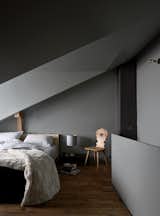 Like the stübli, the top-floor bedroom is meant to be moody. Tuckey designed the bed, the brass wall light is by John Glew Architects, and the chair is another piece inherited from the previous owners, a couple who lived there for decades.  Photo 10 of 12 in A Sliced-Up House Comes Together Again