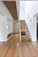 A staircase forms the core of the 1,800-square-foot home, with a symmetrical alcove on either side. The steps, hardwood floors, and slatted bridge on the second floor are made of white oak, providing a rich contrast with its white walls.