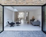 The large patio leads to a newly landscaped back garden. An expansive glass wall promotes seamless indoor-outdoor living. Inexpensive brick pavers were chosen for the rear patio; they offer textural contrast with the steel of the door, brick of the rear facade, and pale gray wood of the interior floors.