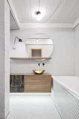 The residents of this maisonette, located in Prague's Vinohrady district, were a young couple returning to the Czech capital after living in London for several years. Stepanova took cues from London's industrial character (with a healthy dash of minimalist design) in devising this remodel's striking aesthetic. In the first bathroom, seen here, a brass washbasin from Morocco is flanked by a Tolomeo Micro Parete lamp from Artemide.  Photo 1 of 7 in Step Aside, Subway Tile—Penny Tile Is the New Classic from A Sleek Kitchen and Double Bathroom Renovation in Prague