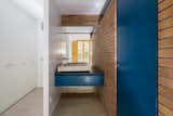 The kitchen sink from the original building was repurposed for the bathroom, with a custom vanity that continues the blue scheme. The space is enclosed by walls of water-repellant brick.