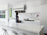Onda barstools by Stua from Design Within Reach surround a 13-foot Calacatta marble island. Custom white aluminum cabinets float above the kitchen appliances by Miele with a stovetop from Wolf and a range hood by Airmec Bello.