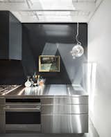 A close-up of the steel counter shows the Artemide Miconos lamp hanging near the sink, as well as the diffused light that streams in via a set of skylights arranged throughout the roof.  Search “atelier-by-mirage.html” from Could You Find Your Dream Home in an Old Abandoned Workshop?