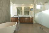 The master bathroom features a spacious vanity area and a frosted glass shower. A blue lava stone wall and Almond bathtub by Porcelanosa add a soft touch in the otherwise linear bathroom.