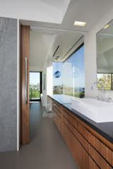 The bathroom counter extends into the bedroom as a desk. A sliding door can fit on a track between the bathroom countertop and bedroom desk to seamlessly partition the two rooms. A blue Niche Modern pendant light adds flair to the bedroom.
