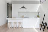 Kitchen, White Cabinet, Light Hardwood Floor, Glass Tile Backsplashe, Marble Counter, Undermount Sink, Pendant Lighting, and Range Black-rimmed steel clerestory windows add illumination in this diminutive white kitchen where black accents abound. A black Aggregato Saliscendi Suspension light, designed by Enzo Mari and Giancarlo Fassina for Artemide, accents against the white Calacatta marble countertops and MAP's oak Milky Stools.  Photo 4 of 8 in Seclusion by Caroline Wallis